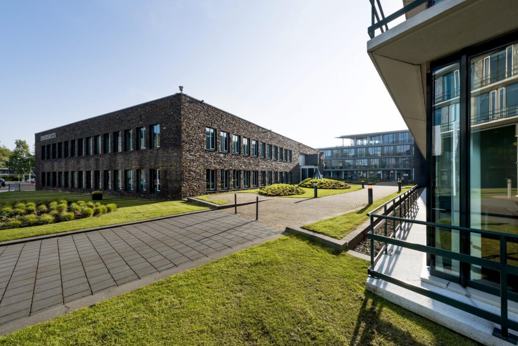 Modern kantoorpand aan de De Cuserstraat met een stenen gevel, grote ramen en een verzorgde buitenruimte.